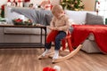 Adorable toddler playing on reindeer rocking by christmas tree at home