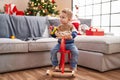 Adorable toddler playing on reindeer rocking by christmas tree at home