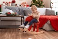 Adorable toddler playing on reindeer rocking by christmas tree at home