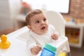 Adorable toddler sitting on baby highchair drinking water at kindergarten