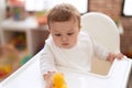 Adorable toddler sitting on baby highchair holding rubber duck toy at kindergarten