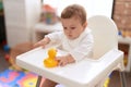 Adorable toddler sitting on baby highchair holding rubber duck toy at kindergarten