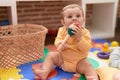 Adorable toddler sucking maraca sitting on floor at kindergarten