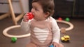 Adorable toddler sucking plastic ball sitting on floor at kindergarten