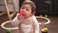 Adorable toddler sucking plastic ball sitting on floor at kindergarten