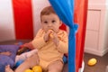 Adorable toddler sucking toy sitting on floor inside cirus tent at home