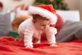 Adorable toddler wearing christmas hat crawling on sofa at home