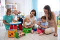 Adorable toddlers playing with colorful toys and mothers in nursery room. Nursery babies playing with adults in day care Royalty Free Stock Photo