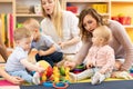 Adorable toddlers playing with colorful toys and mothers in nursery room Royalty Free Stock Photo