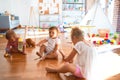 Adorable toddlers sitting on the floor playing around lots of toys at kindergarten