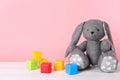 Adorable toy bunny and plastic cubes on table against color background, space for text.
