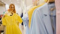 Adorable woman in a clothing store chooses a yellow dress - shopping concept Royalty Free Stock Photo
