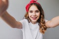 Adorable woman in red vintage ribbon making selfie. Debonair white girl with curly hair posing with