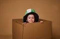 Adorable 4 year old child girl with a Leprechaun hat peeks out from under a cardboard box and smiles cutely at the camera. Happy Royalty Free Stock Photo