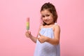 Adorable 4 years pretty baby girl holding healthy vegan ice cream popsicle in hand and showing thumb up , posing on pink wall Royalty Free Stock Photo