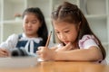 An adorable young Asian elementary school girl is focusing on studying, writing, or drawing Royalty Free Stock Photo