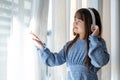 An adorable young Asian girl in a blue dress is daydreaming while listening to music on headphones Royalty Free Stock Photo