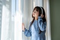 An adorable young Asian girl in a blue dress is daydreaming while listening to music on headphones Royalty Free Stock Photo