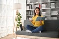 Adorable young Asian girl drinking a cup of coffee while reading book on sofa Royalty Free Stock Photo