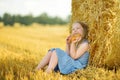 Adorable young girl eating pretzel in a wheat field on a summer day. Child playing at hay bale field during harvest time. Kid Royalty Free Stock Photo