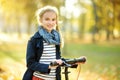 Adorable young girl riding her scooter in a city park on sunny autumn evening. Pretty preteen child riding a roller
