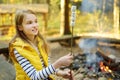 Adorable young girl roasting marshmallows on stick at bonfire. Child having fun at camp fire. Camping with children in fall forest Royalty Free Stock Photo