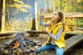 Adorable young girl roasting marshmallows on stick at bonfire. Child having fun at camp fire. Camping with children in fall forest