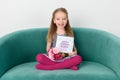 Adorable young girl sitting on a couch, holding bouquet of pink gerbera daisies and Mother`s day card. Happy Mother`s Day.