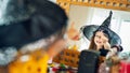 Adorable young girl wearing witch hat looking at herself in the mirror, pointing with finger and laughing. Royalty Free Stock Photo