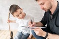 Adoult man writes notes of simple melody on music sheet for his younger brother, who learn to play guitar