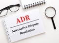 ADR Alternative Dispute Resolution is written in a white notebook on a light background near the notebook, black-framed glasses Royalty Free Stock Photo