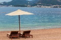 Adriatic sea summer beach. Wooden chairs and umbrella on pebble beach by blue water. Montenegro, Budva riviera Royalty Free Stock Photo