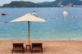 Adriatic sea summer beach. Wooden chairs and umbrella on pebble beach by blue water. Montenegro, Budva riviera Royalty Free Stock Photo