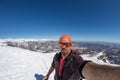 Adult alpin skier with beard, sunglasses and hat, taking selfie on snowy slope in the beautiful italian Alps with clear blue sky.