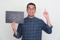 Adult Asian man pointing up with excited expression while holding paper with 2023 text Royalty Free Stock Photo