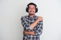 Adult Asian man showing relieved gesture when listening music using headset and hugging himself