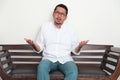 Adult Asian man sitting in a couch showing confused expression Royalty Free Stock Photo