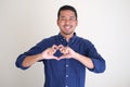 Adult Asian man smiling while giving heart shape symbol using fingers