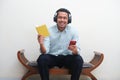 Adult Asian man smiling happy to camera when listening music with both hand holding handphone and book Royalty Free Stock Photo