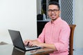 Adult Asian man smiling while working using laptop in his home Royalty Free Stock Photo