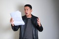 Adult Asian man wearing black leather jacket showing shocked expression when read document Royalty Free Stock Photo