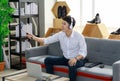 Adult asian man wearing white shirt sitting at gray sofa wearing headphone holding gimbal stabilizer with smartphone doing live to