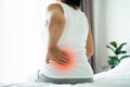 Adult Asian woman is sitting on the bed and holding her lower back suffering from injured back. Health care and back pain concept Royalty Free Stock Photo