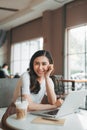 Adult asian woman in white shirt sitting at table with laptop Royalty Free Stock Photo