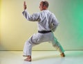 Adult athlete with black belt doing formal exercises against color background with yellow and green tint Royalty Free Stock Photo