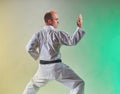 An adult athlete with a black belt performs formal exercises against a colored background with yellow and green tints Royalty Free Stock Photo