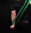 Adult athlete in black uniform stands with his back and stretches a green sports elastic band