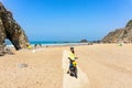 Adult attractive female cyclist with her bike is posing and smiling on a ocean beach. Portugal, Europe