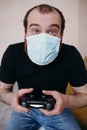 Adult balding white man playing video games with medical mask on his face while Covid-19 quarantine Royalty Free Stock Photo