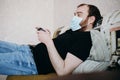 Adult balding white man playing video games with medical mask on his face while Covid-19 quarantine Royalty Free Stock Photo